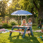Two children sitting at a colorful picnic table with a striped umbrella in a garden setting.