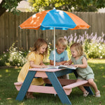 Three children sitting at a colorful picnic table under an umbrella in a garden.