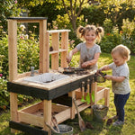 Two children playing with a wooden outdoor play kitchen set in a garden.